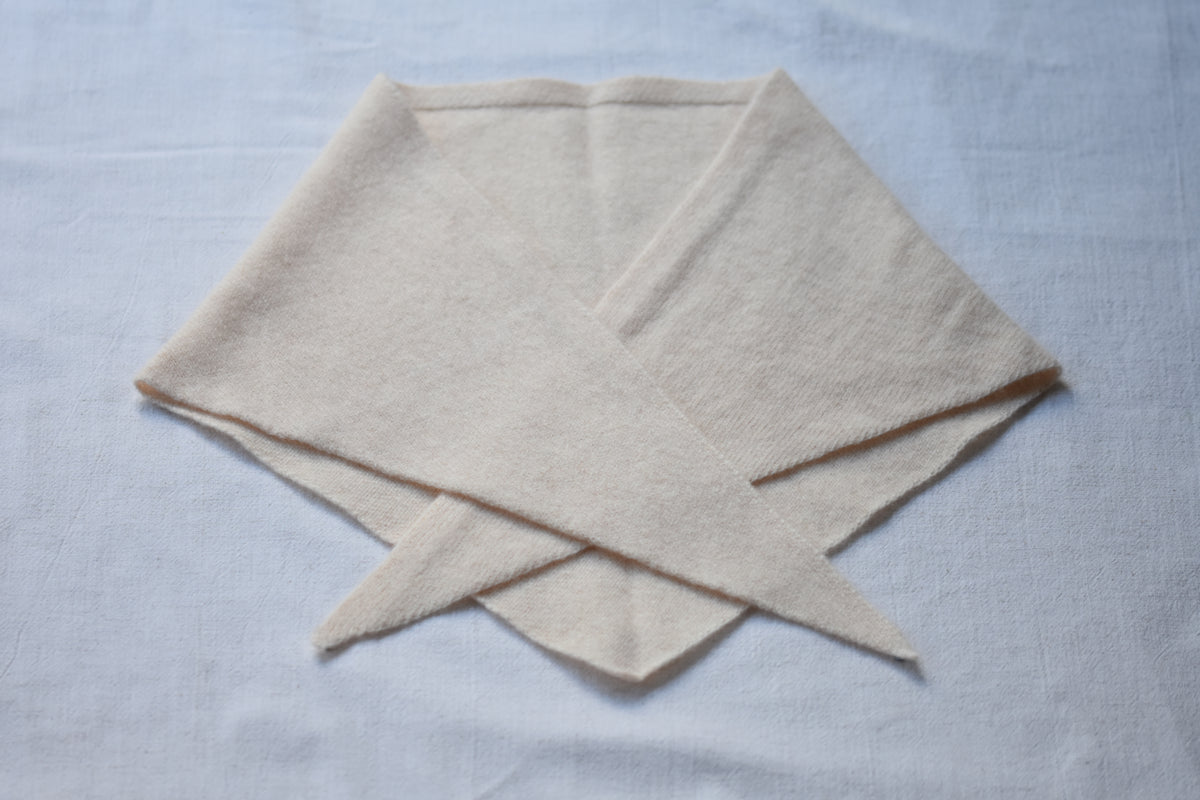 Cream marl Merino wool triangle scarf by Roake Studio lay flat and crossed over on a beige background.