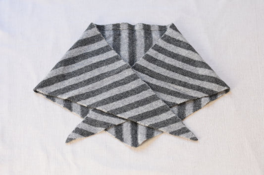 Grey and charcoal striped Merino wool triangle scarf by Roake Studio lay flat and crossed over on a beige background.