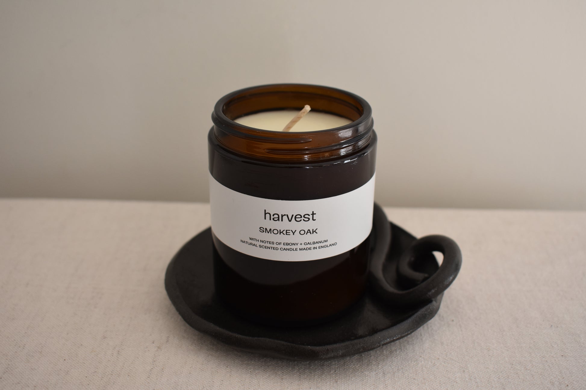 Harvest Smokey Oak candle in brown glass vessel on We Are Clay black ceramic spiral Wee Dish.