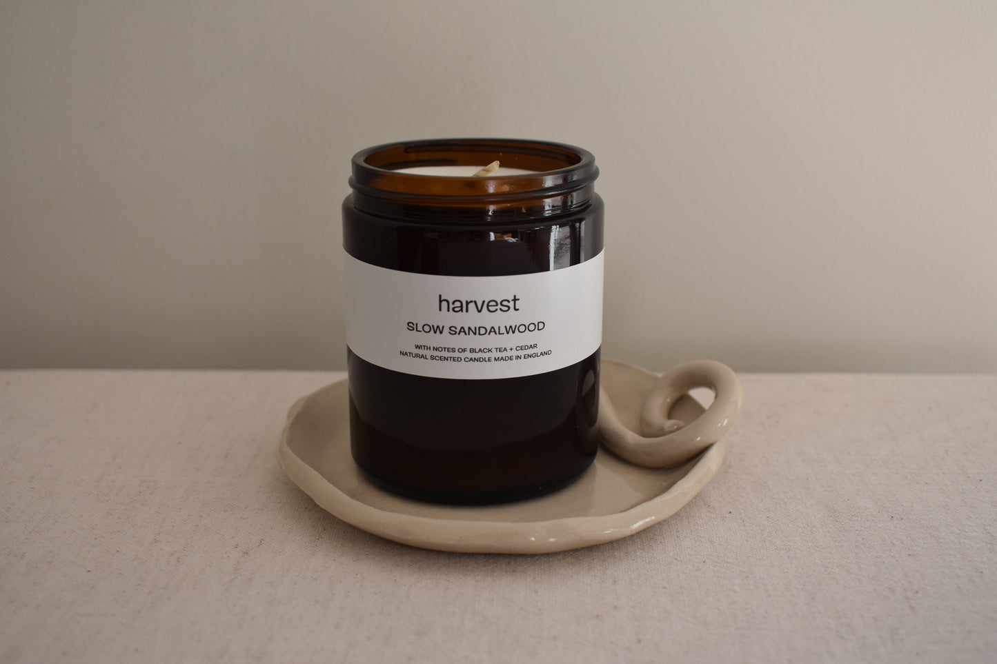 Harvest Slow Sandalwood candle in brown glass vessel on We Are Clay white ceramic spiral Wee Dish.