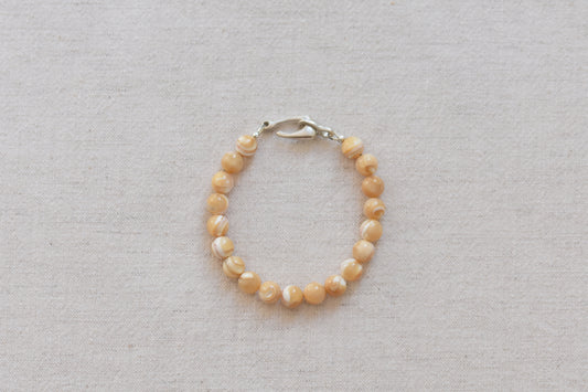 By my hands Sandy Bei Bracelet of opalescent light yellow Mother of Pearl beads, with a hand-carved sterling silver fish hook closure, on a beige background.