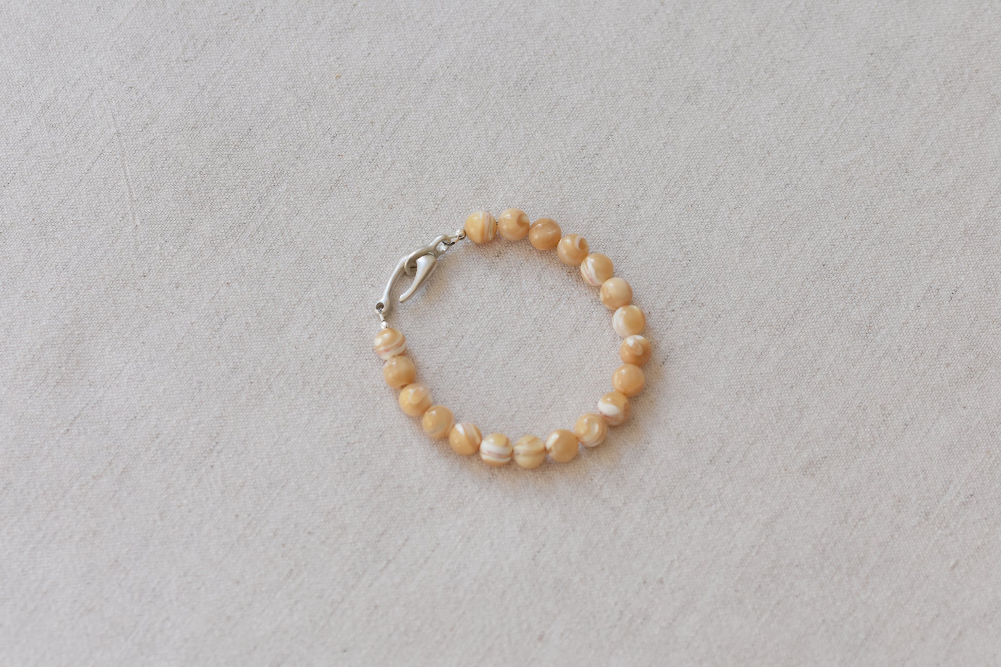 By my hands Sandy Bei Bracelet of opalescent light yellow Mother of Pearl beads, with a hand-carved sterling silver fish hook closure, on a beige background.