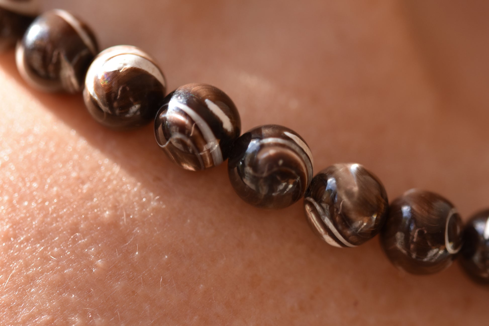 By my hands Burnt Umber Bei Necklace of opalescent dark brown Mother of Pearl beads, close up, shown on a person.