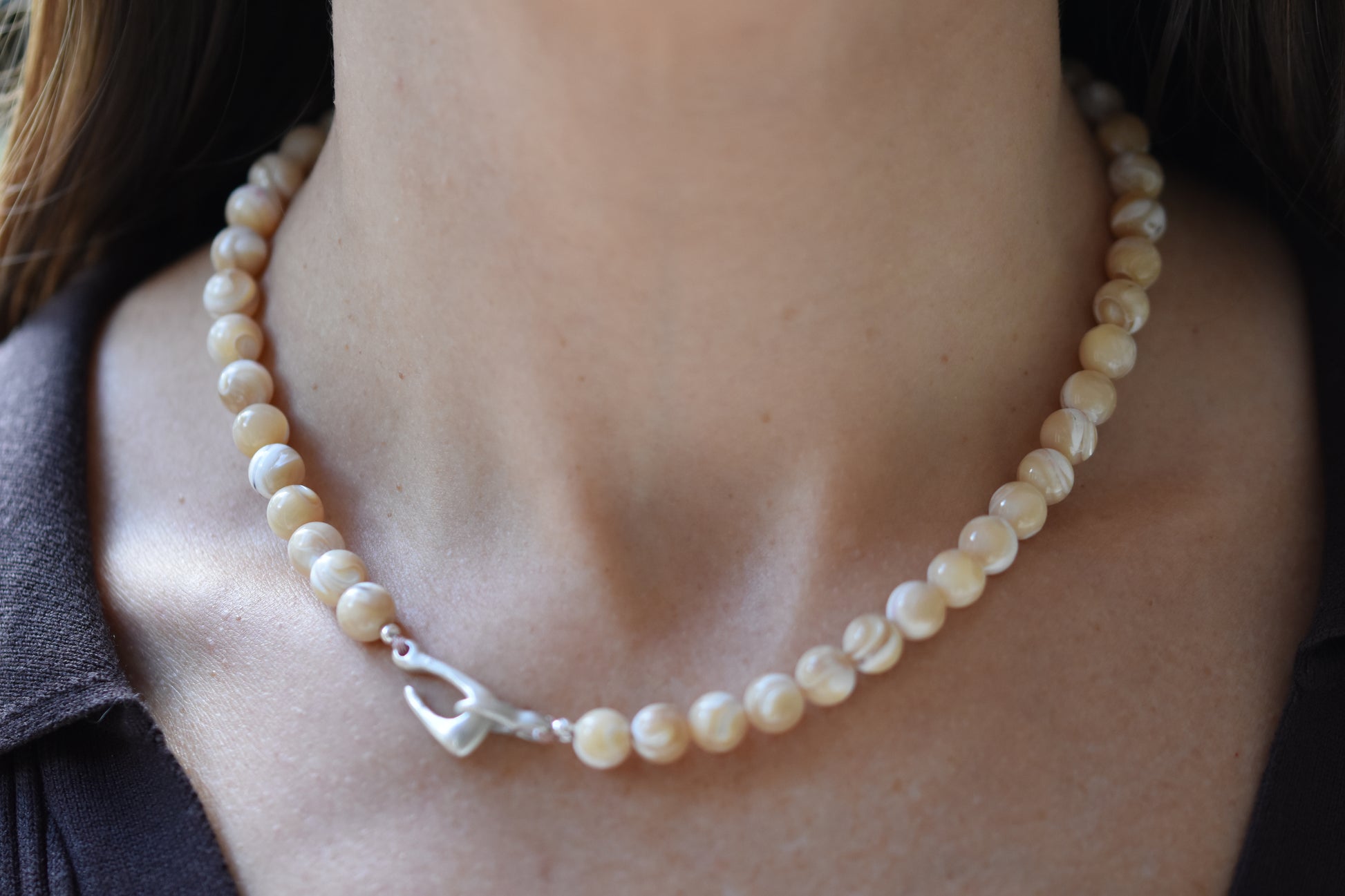 By my hands Sandy Bei Necklace of opalescent light yellow Mother of Pearl beads, with a hand-carved sterling silver fish hook closure shown on a person.