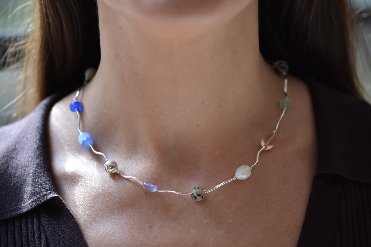 By my hands Fluorescence Ripple Necklace with wavy sterling silver ripples and gemstone beads including peridot, dalmatian jasper, freshwater pearl, and coloured jade, shown on a person.