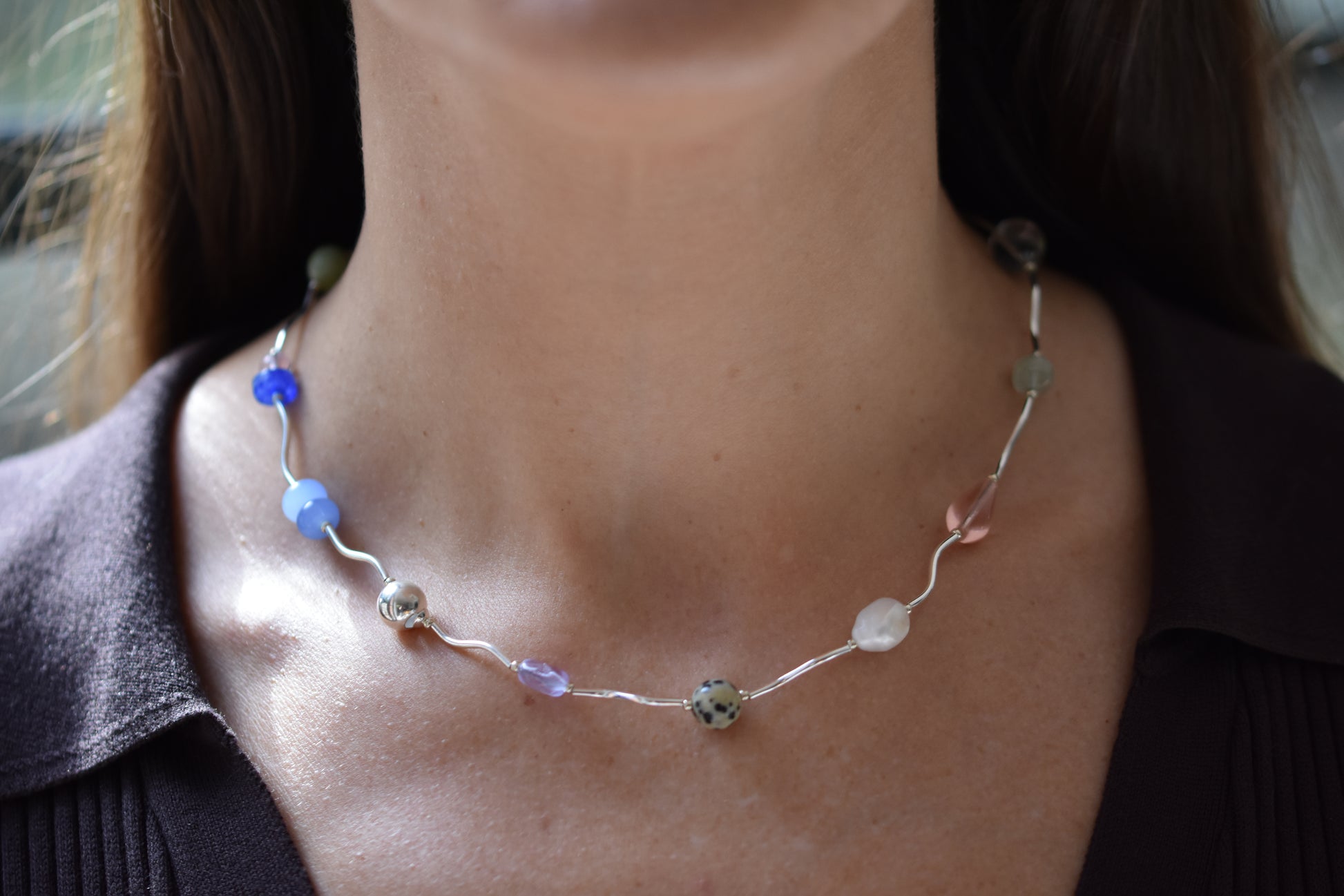 By my hands Fluorescence Ripple Necklace with wavy sterling silver ripples and gemstone beads including peridot, dalmatian jasper, freshwater pearl, and coloured jade, shown on a person.