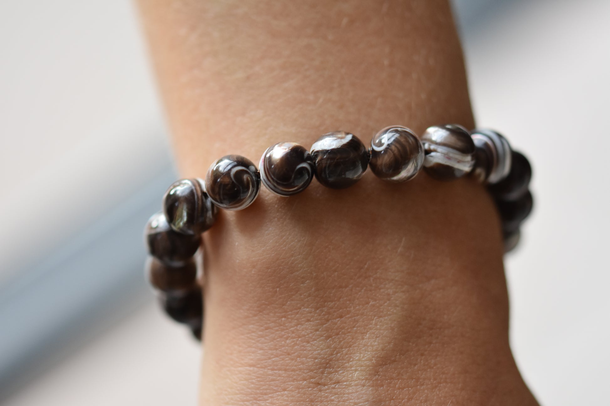 By my hands Burnt Umber Bei Bracelet of opalescent dark brown Mother of Pearl beads, shown on a person.