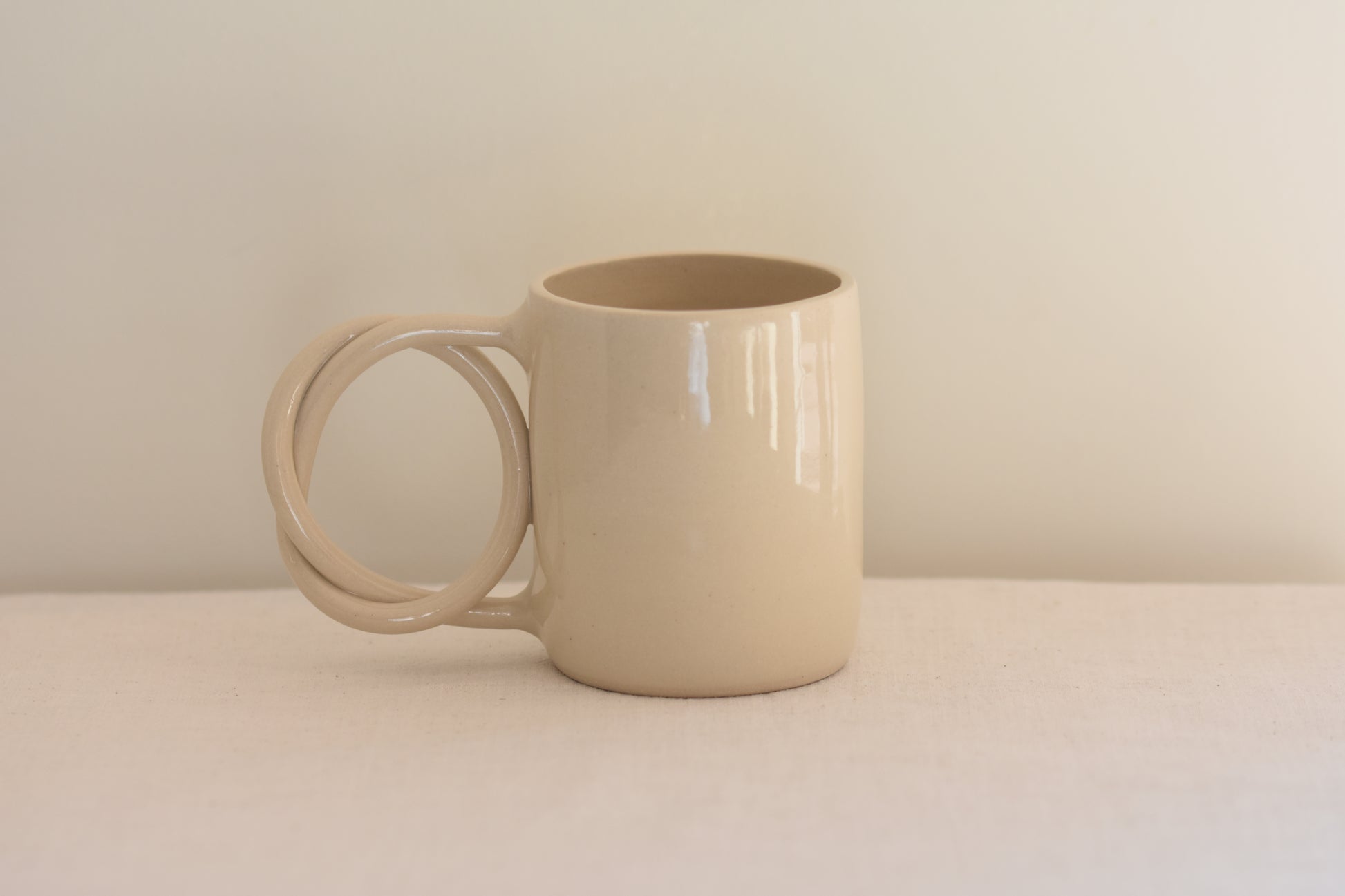 We Are Clay white ceramic mug with pretzel shaped handle on a beige background.