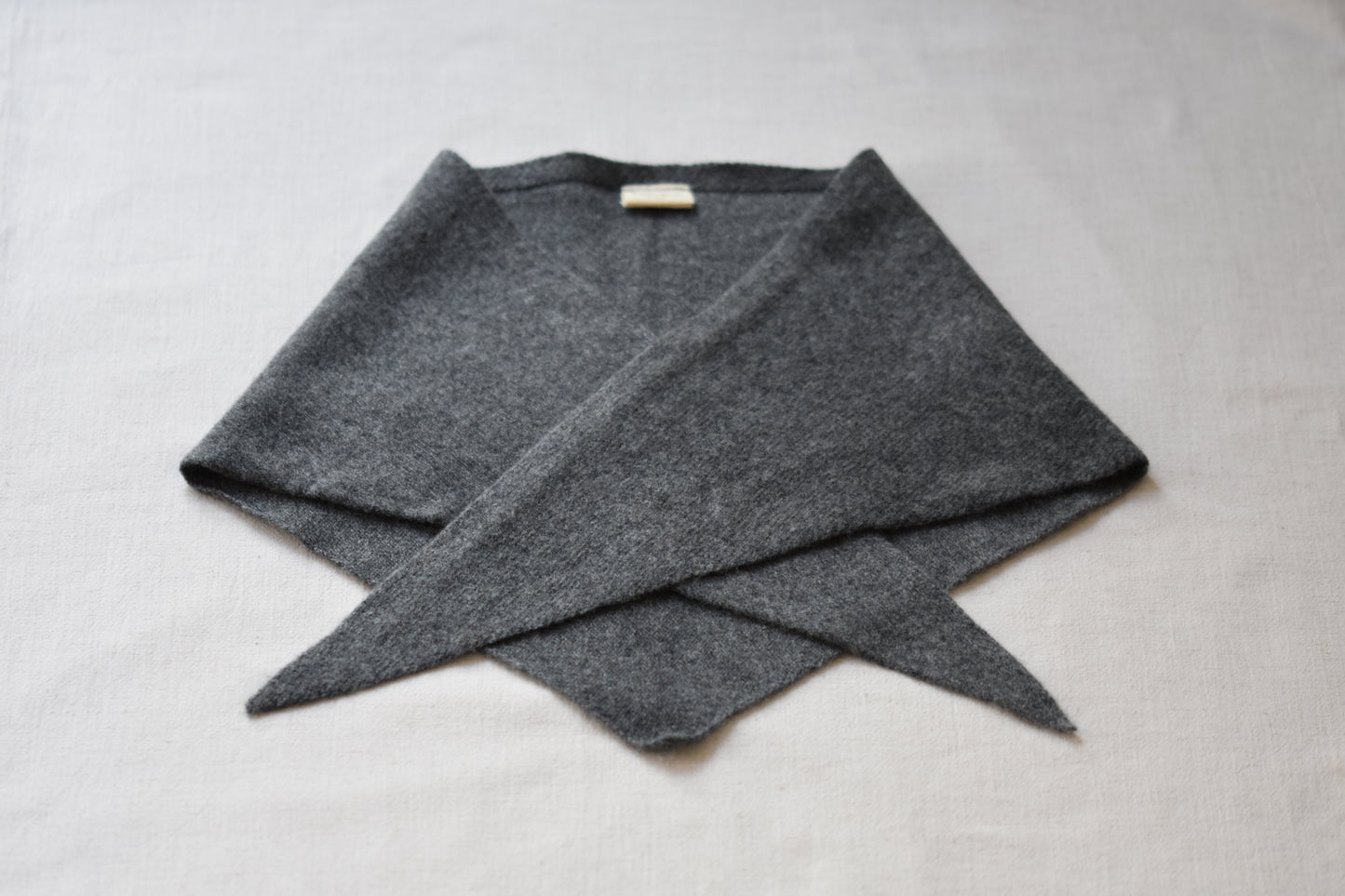 Roake Studio grey merino wool triangle scarf folded on a beige background.