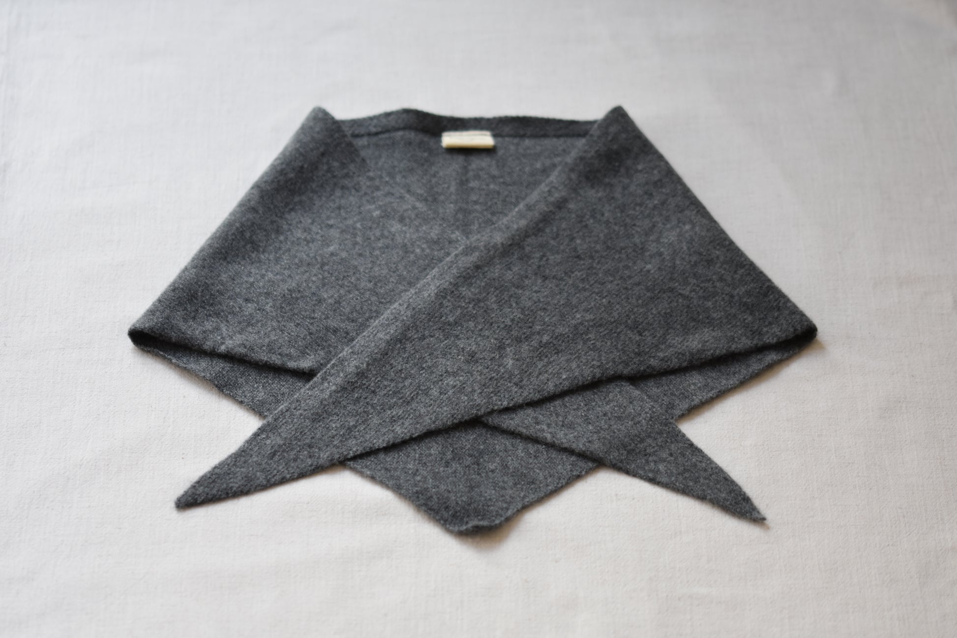 Roake Studio grey merino wool triangle scarf folded on a beige background.