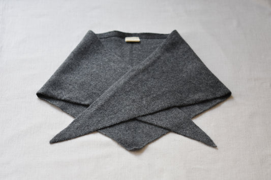 Roake Studio grey merino wool triangle scarf folded on a beige background.
