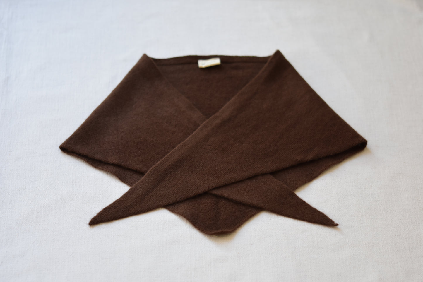 Roake Studio brown merino wool triangle scarf folded on a beige background.
