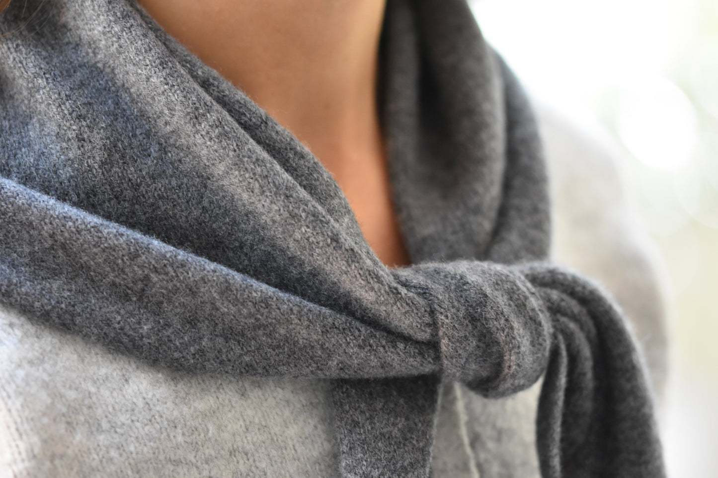 Roake Studio grey merino wool triangle scarf with front knot, close up, worn by a person in a grey cardigan.