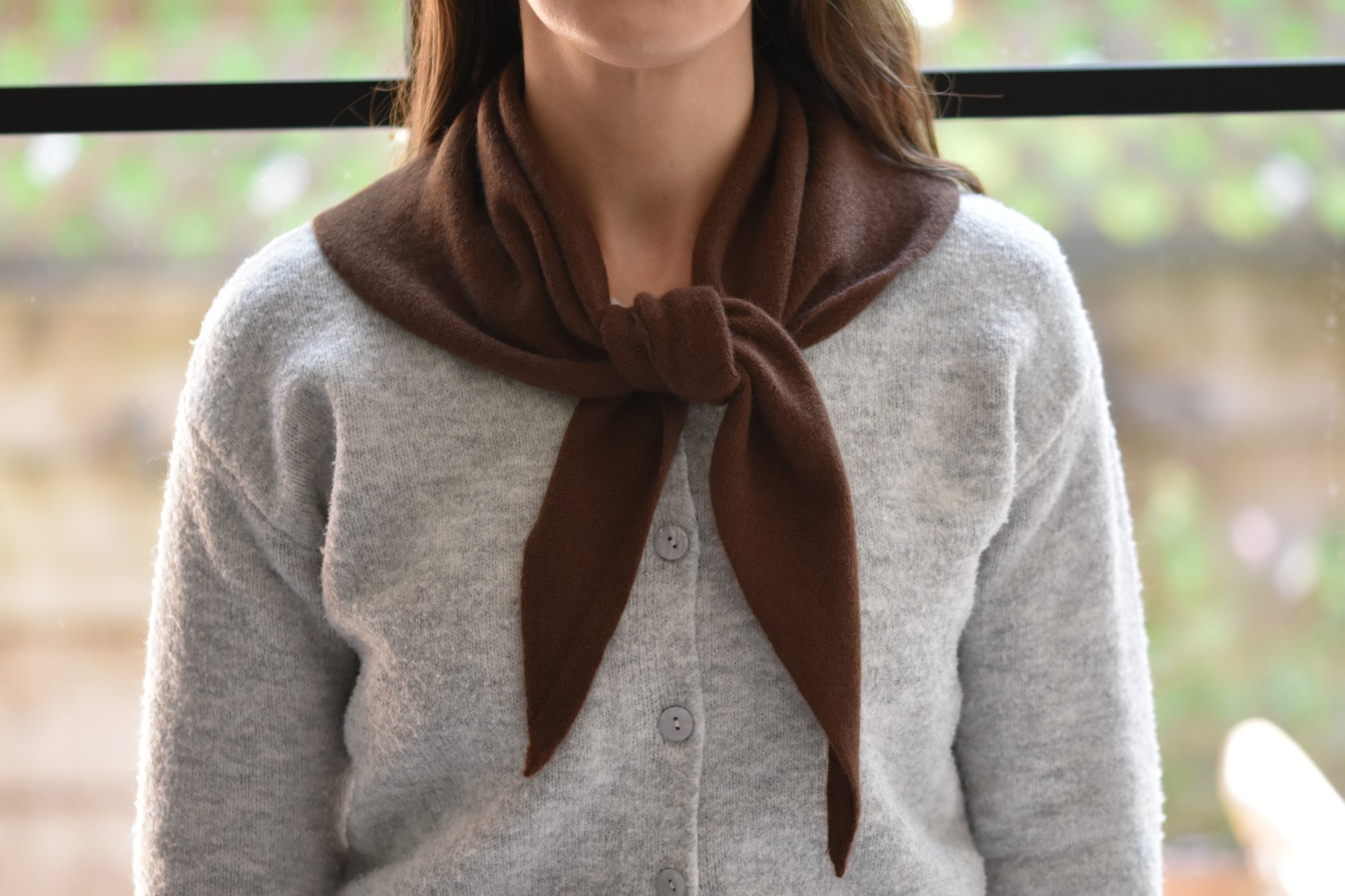 Roake Studio brown merino wool triangle scarf with front knot, worn by a person in a grey cardigan.