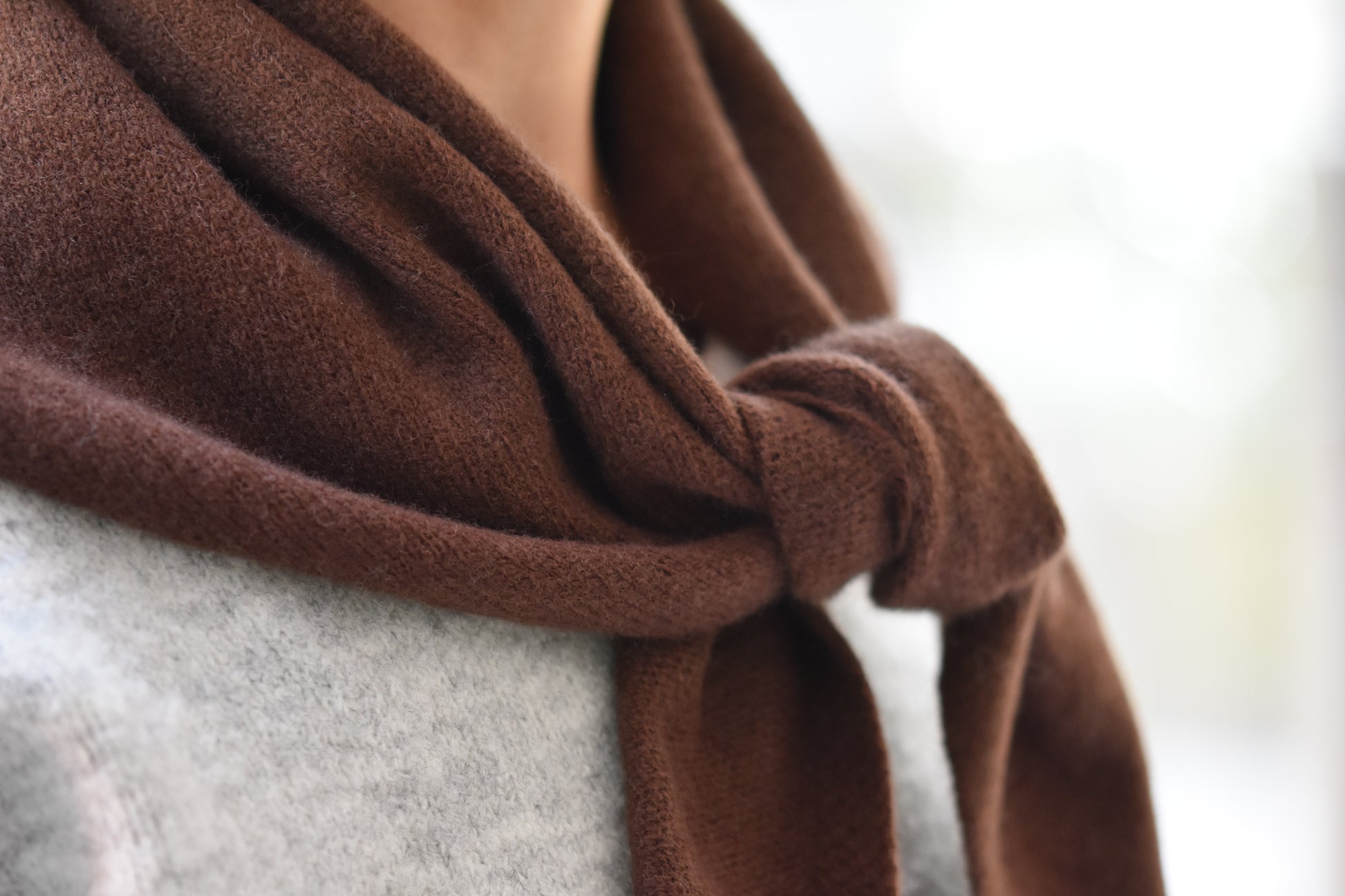 Roake Studio brown merino wool triangle scarf with front knot, close up, worn by a person in a grey cardigan.