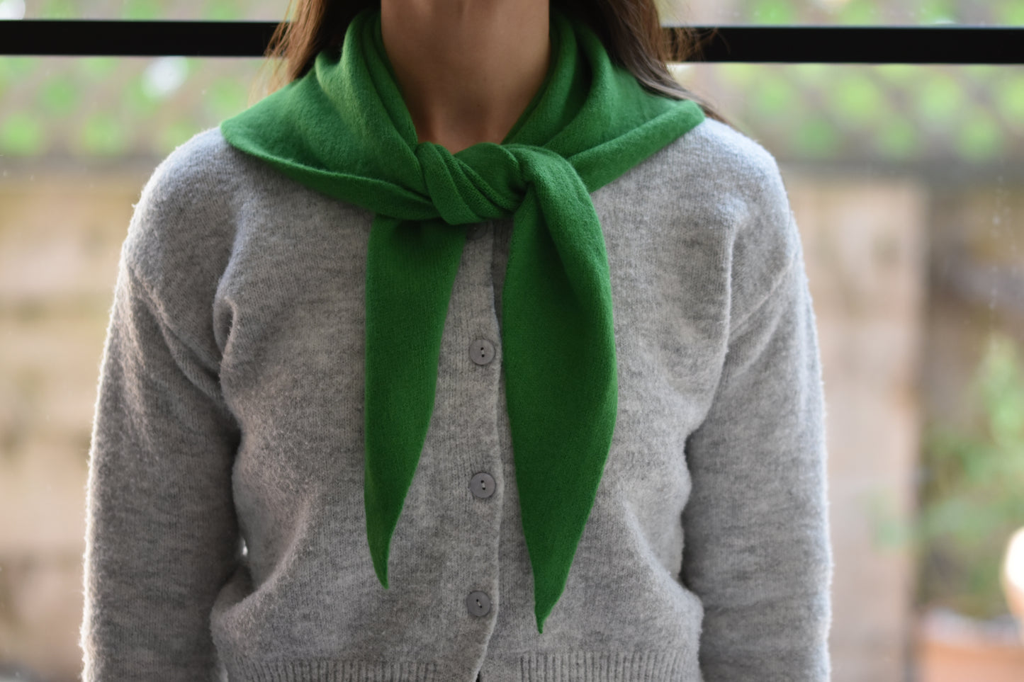 Roake Studio green merino wool triangle scarf with front knot, worn by a person in a grey cardigan.