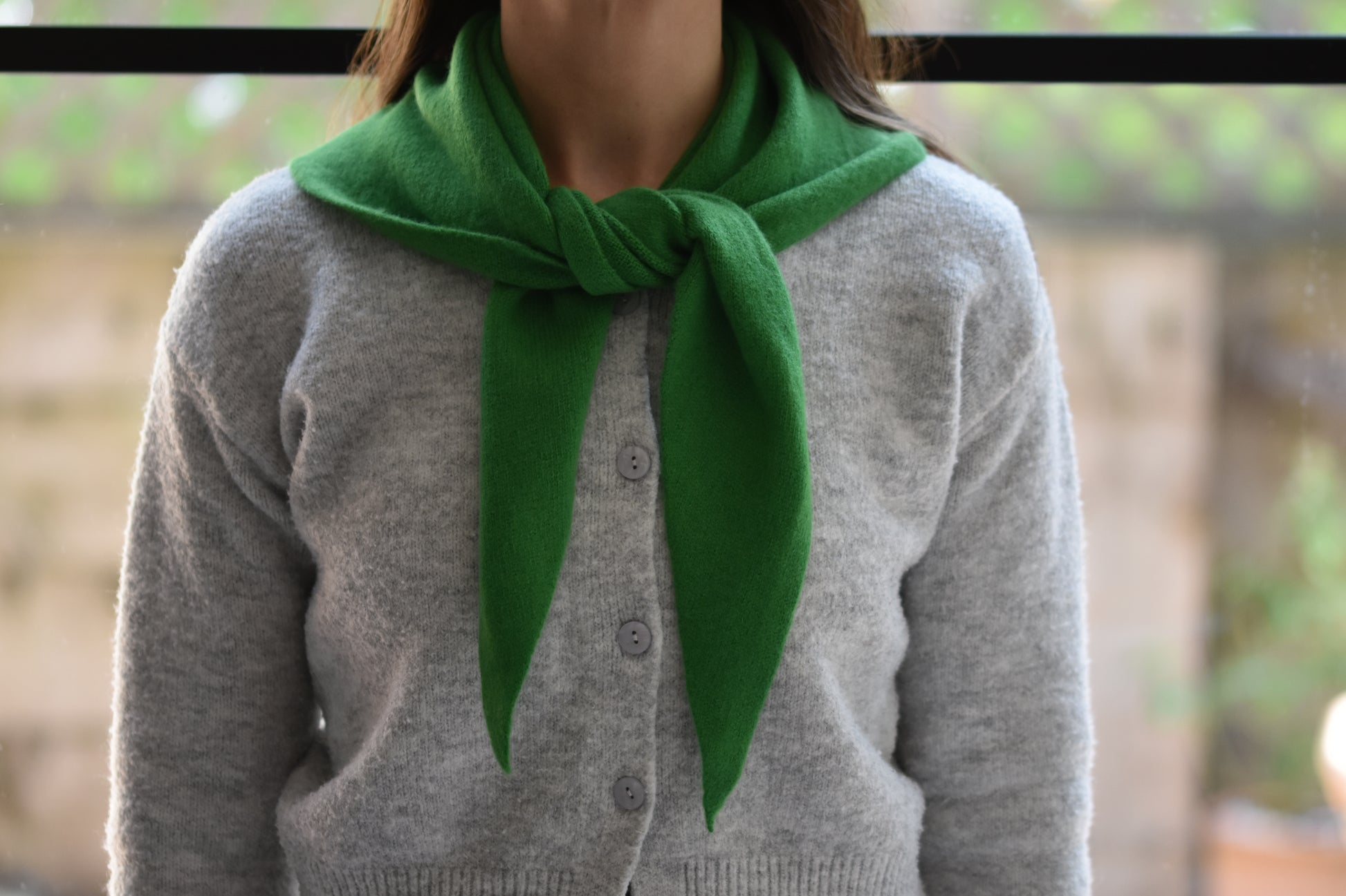 Roake Studio green merino wool triangle scarf with front knot, worn by a person in a grey cardigan.
