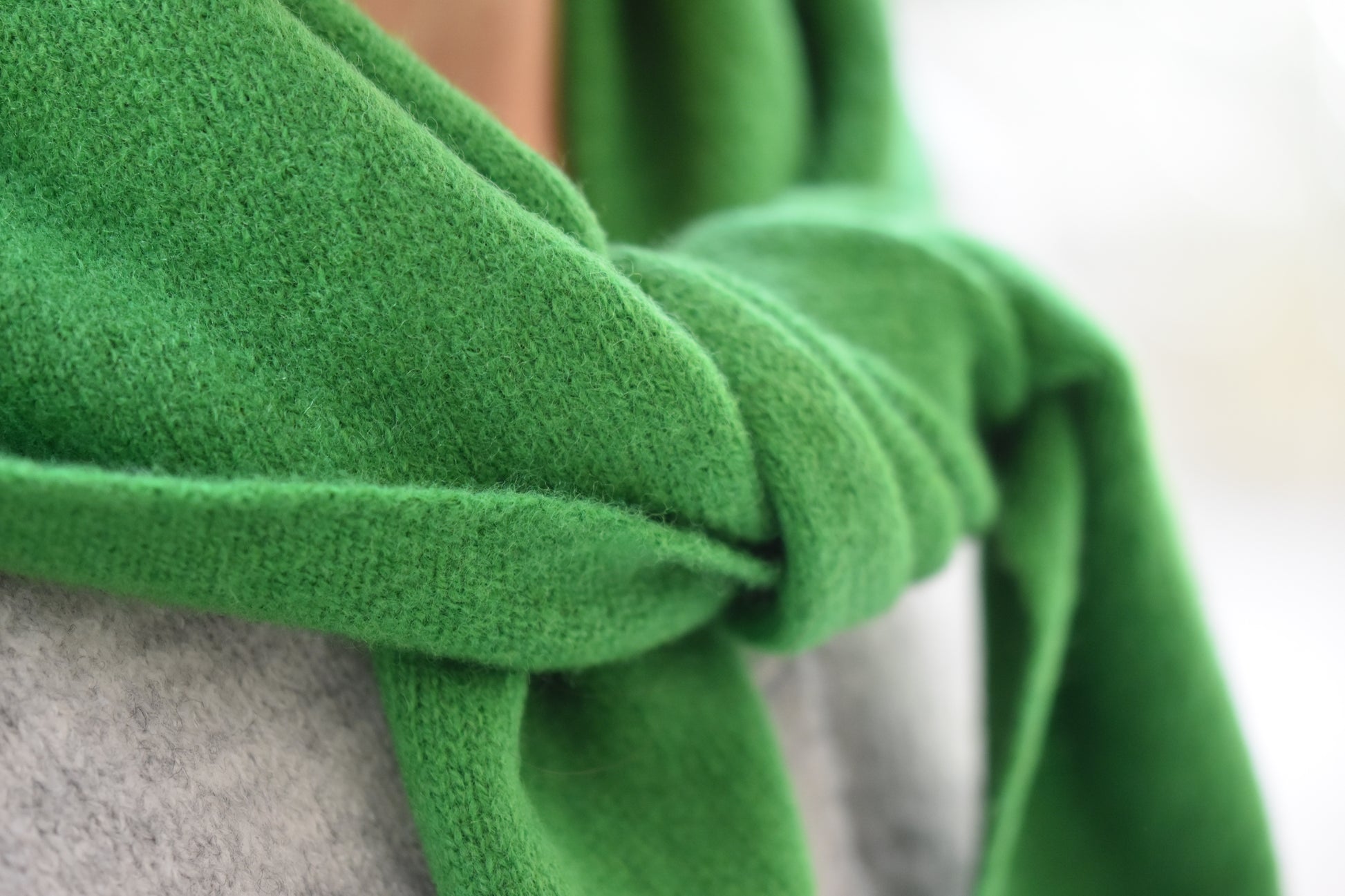 Roake Studio green merino wool triangle scarf with front knot, close up, worn by a person in a grey cardigan.