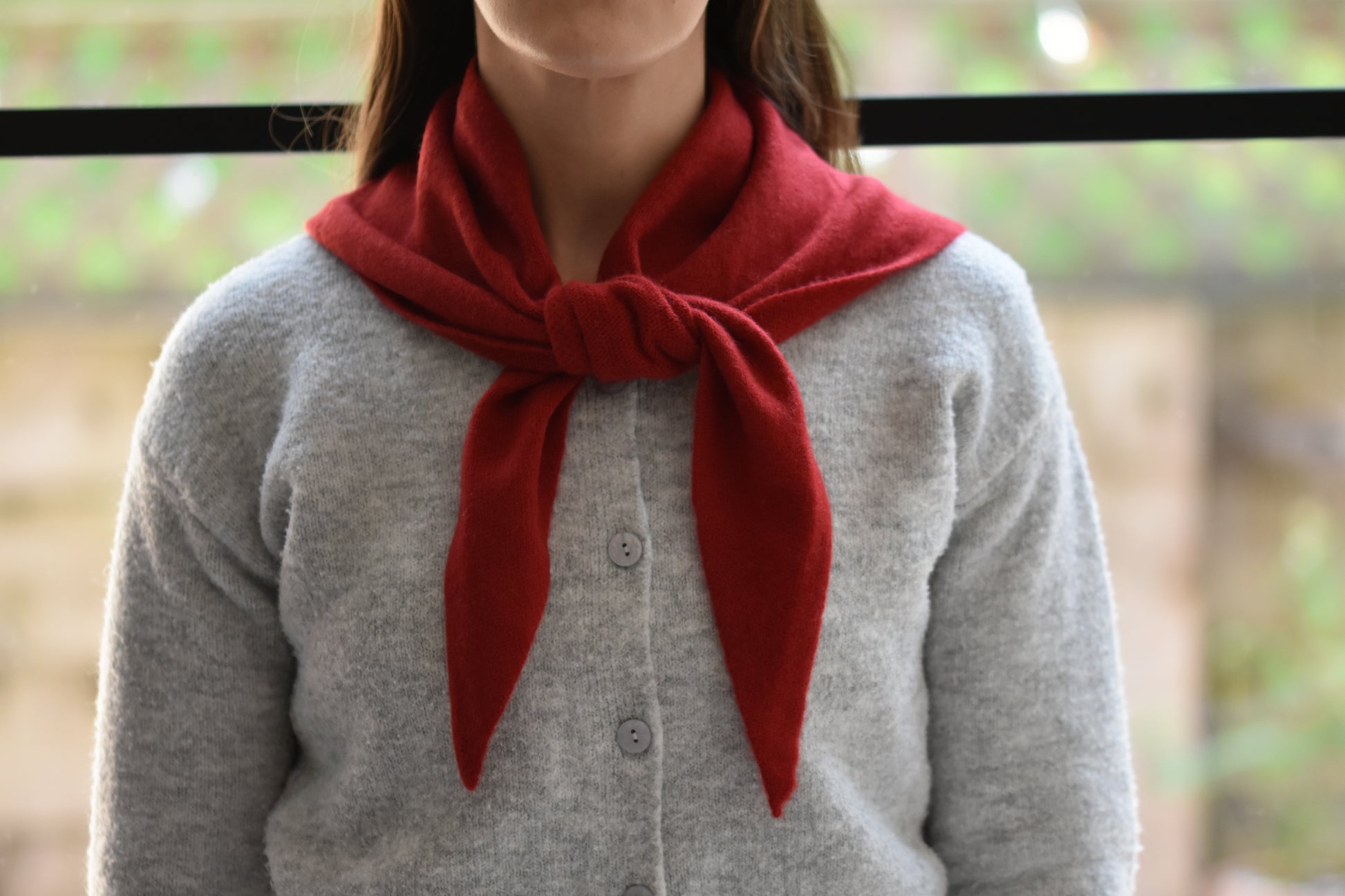 Roake Studio red merino wool triangle scarf with front knot worn by a person in a grey cardigan.