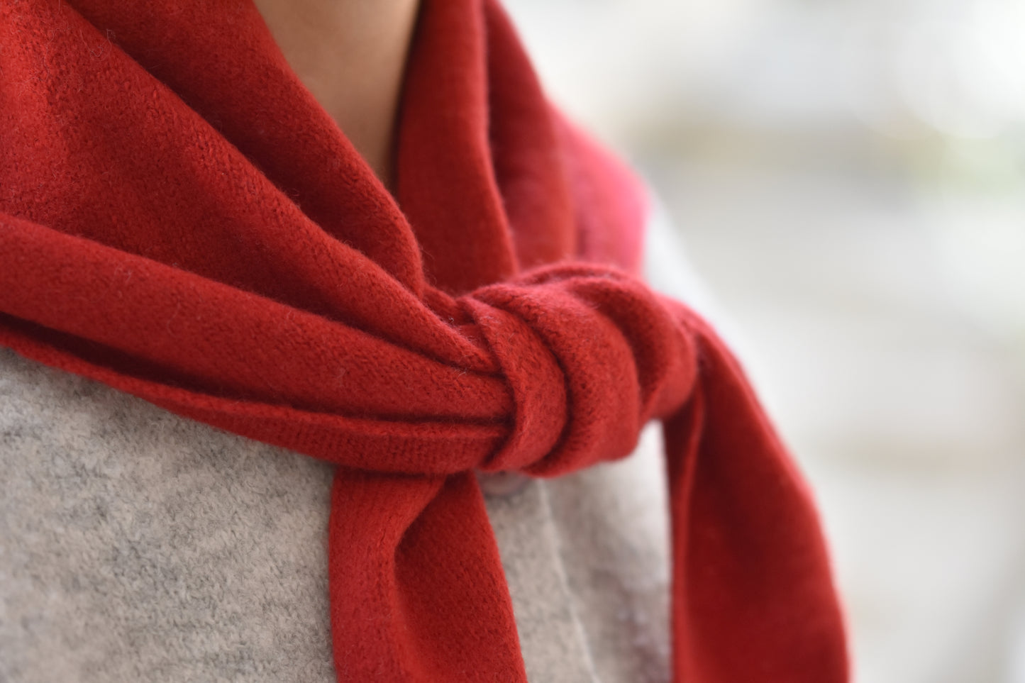 Roake Studio red merino wool triangle scarf with front knot, close up, worn by a person in a grey cardigan.