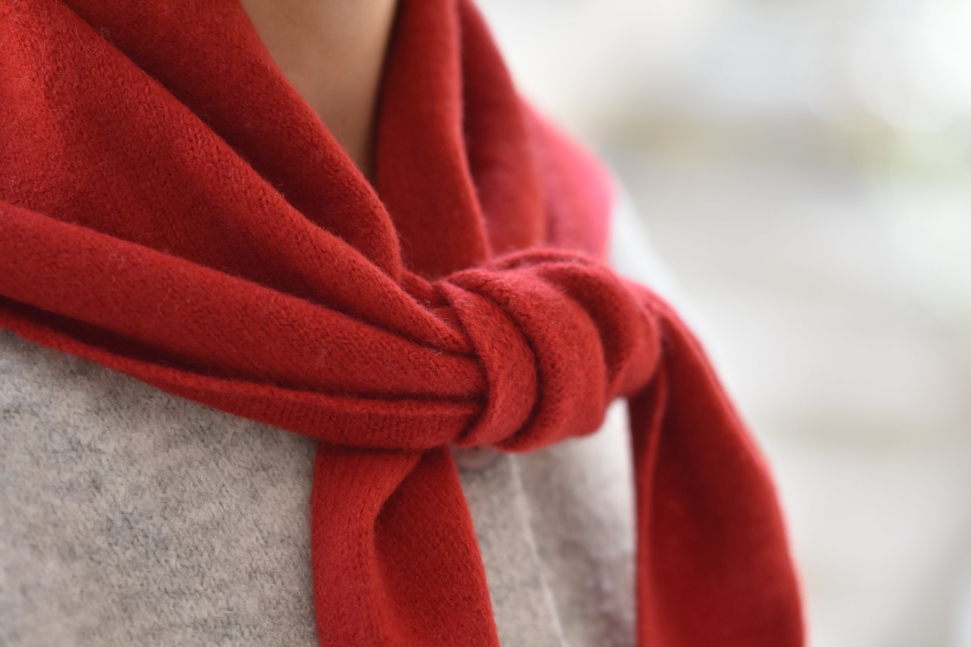 Roake Studio red merino wool triangle scarf with front knot, close up, worn by a person in a grey cardigan.