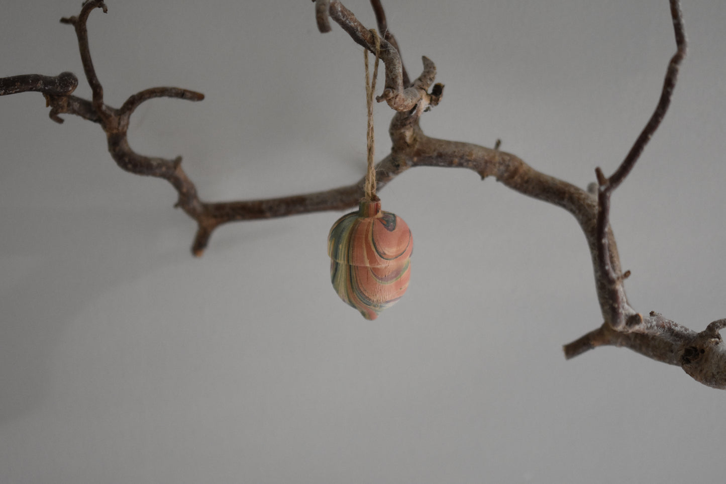 Jemma Lewis marbled wooden decorative acorn hanging from a branch against a white background.