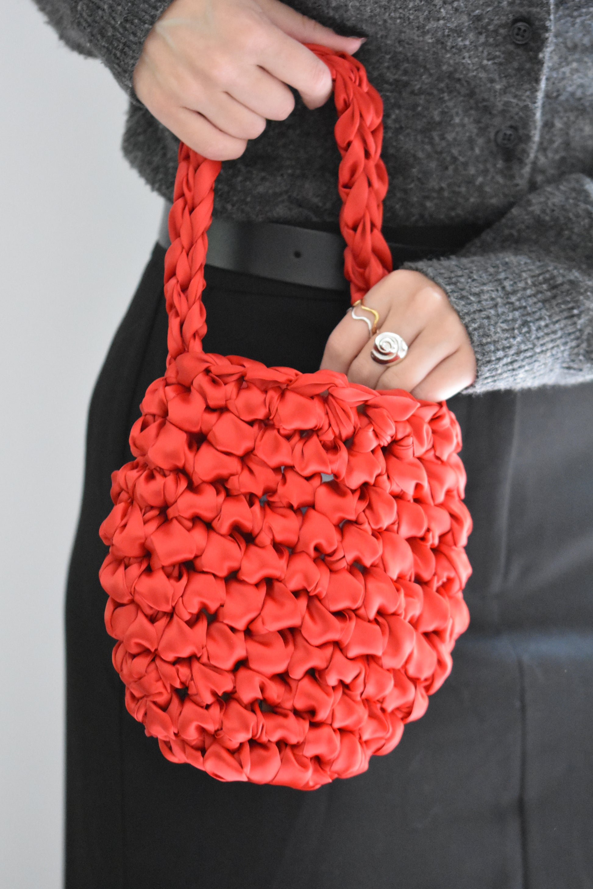 Isla de Gar Hive Bag with crocheted satin ribbon in lipstick red, shown with Hannah Bourn spiral Periwinkle ring in silver and wavy Saccostrea rings in gold and silver.