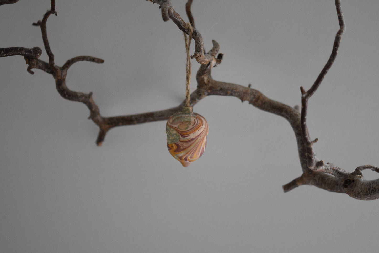 Jemma Lewis marbled wooden decorative acorn hanging from a branch against a white background.