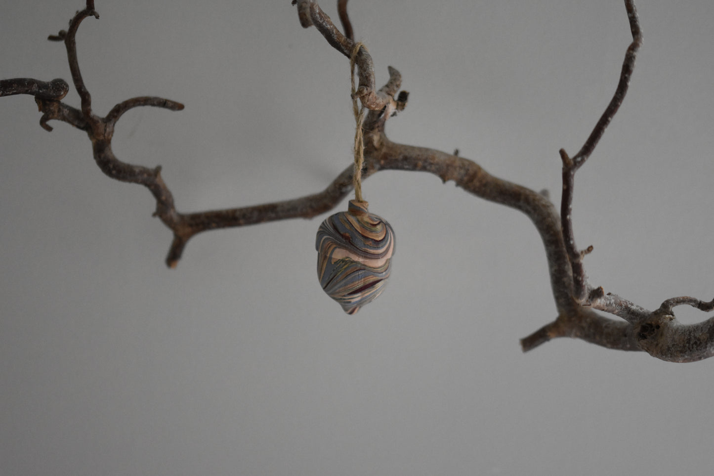 Jemma Lewis marbled wooden decorative acorn hanging from a branch against a white background.