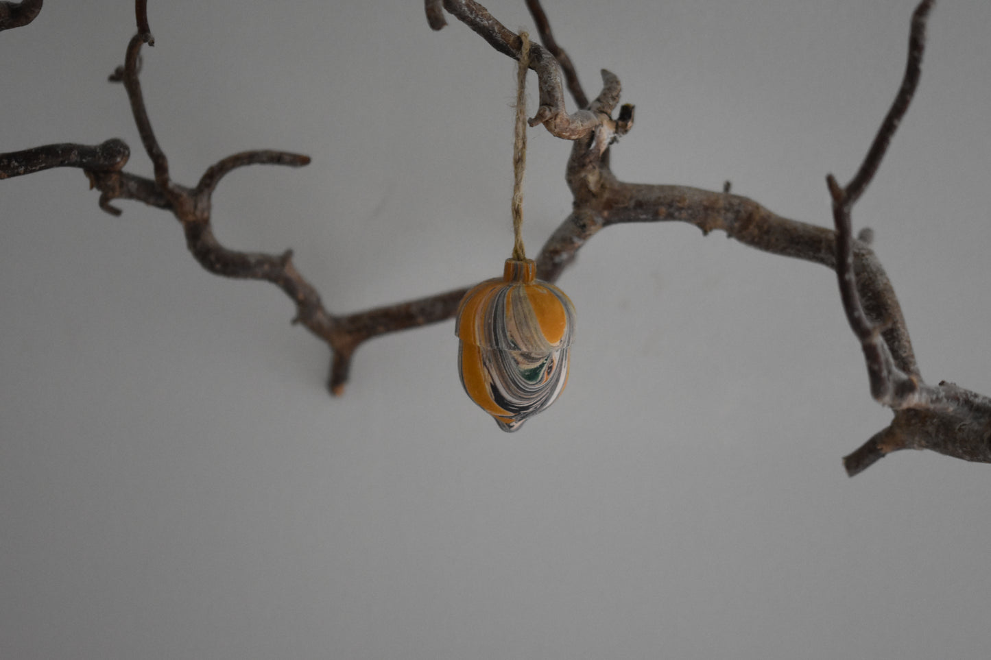 Jemma Lewis marbled wooden decorative acorn hanging from a branch against a white background.