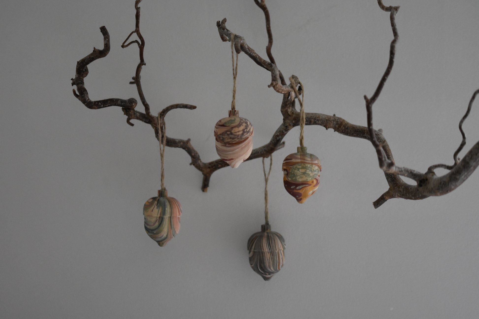 Four Jemma Lewis marbled wooden decorative acorns hanging from a branch against a white background.