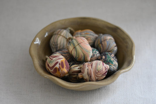 Jemma Lewis marbled decorative wooden acorns in a beige ceramic wavy bowl on a cream background.