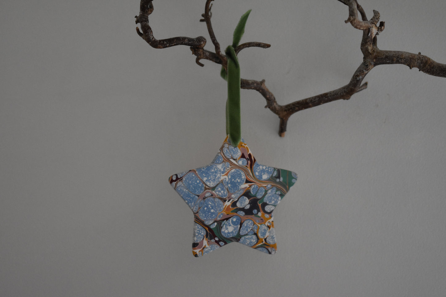Jemma Lewis marbled ceramic star decoration with colourful velvet ribbon hanging on a branch with a white background.