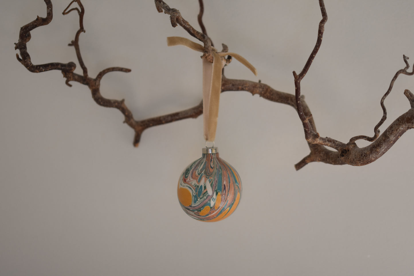 Jemma Lewis colourful marbled round ceramic bauble Christmas ornament with velvet ribbon, hanging from a branch on a white background.