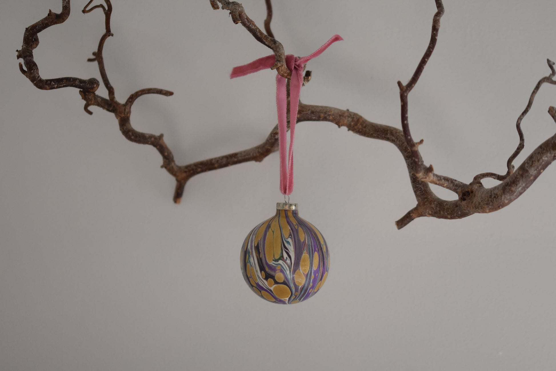 Jemma Lewis colourful marbled round ceramic bauble Christmas ornament with velvet ribbon, hanging from a branch on a white background.