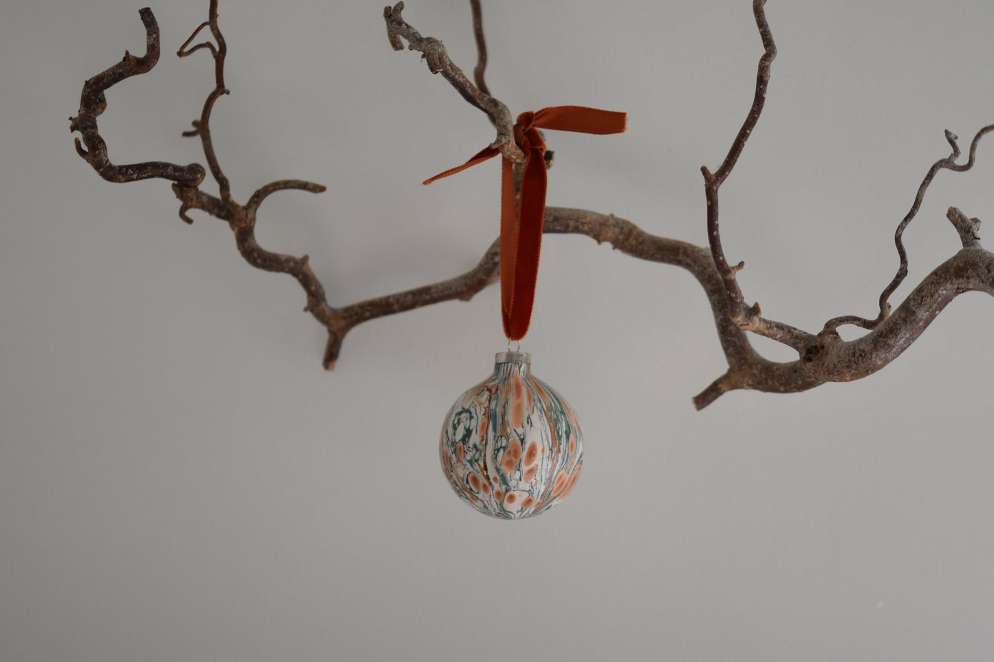 Jemma Lewis colourful marbled round ceramic bauble Christmas ornament with velvet ribbon, hanging from a branch on a white background.