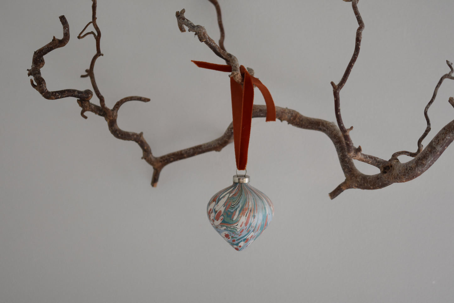 Jemma Lewis colourful marbled teardrop ceramic bauble Christmas ornament with velvet ribbon, hanging from a branch on a white background.