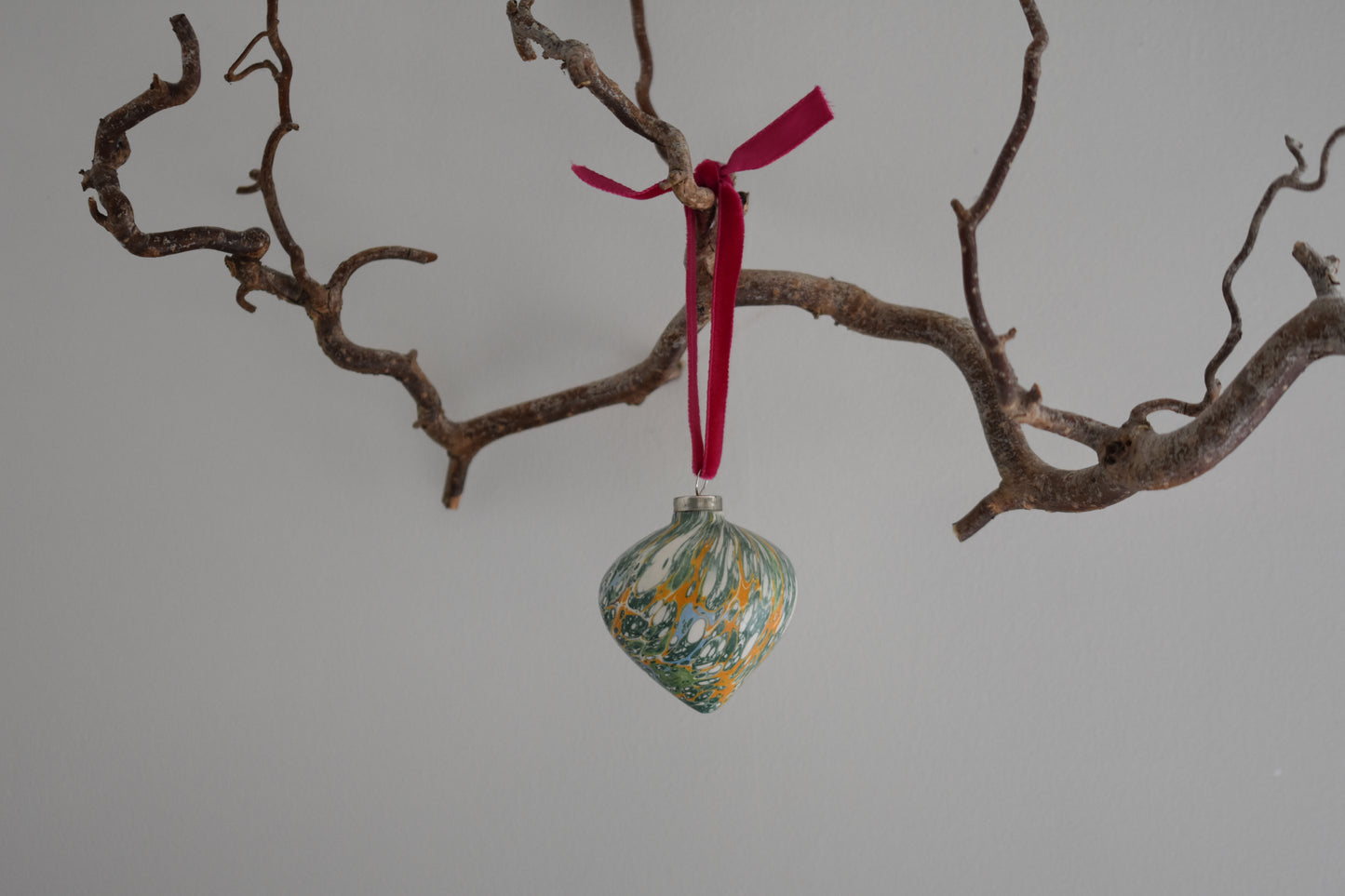 Jemma Lewis colourful marbled teardrop ceramic bauble Christmas ornament with velvet ribbon, hanging from a branch on a white background.