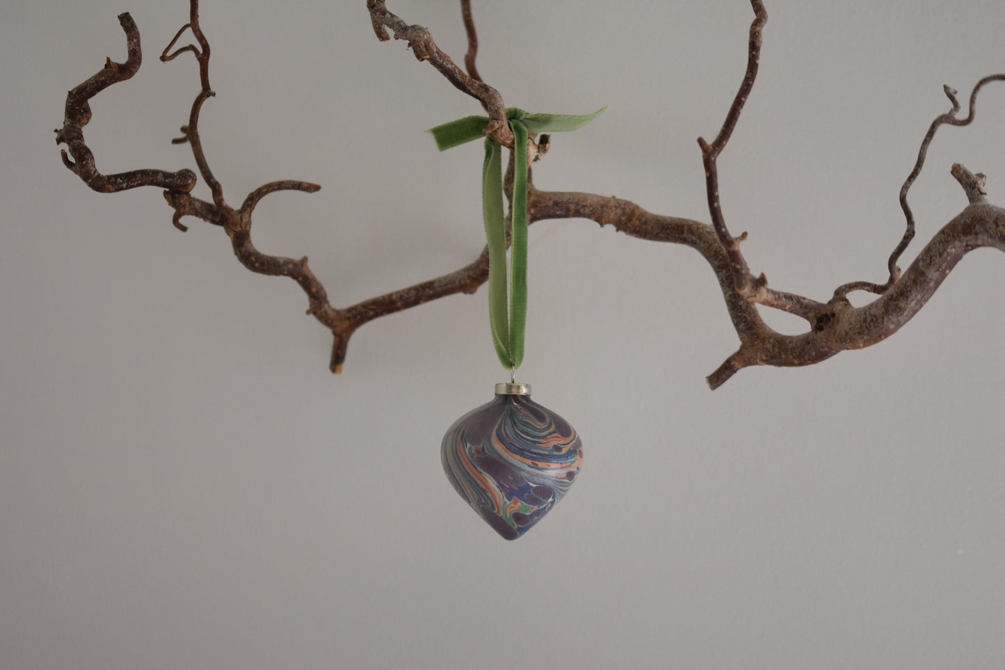 Jemma Lewis colourful marbled teardrop ceramic bauble Christmas ornament with velvet ribbon, hanging from a branch on a white background.