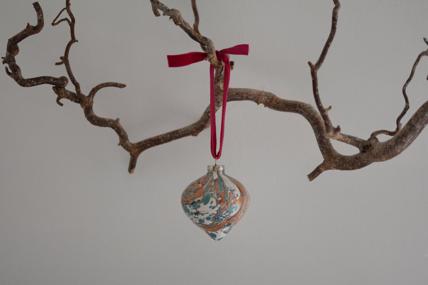 Jemma Lewis colourful marbled teardrop ceramic bauble Christmas ornament with velvet ribbon, hanging from a branch on a white background.