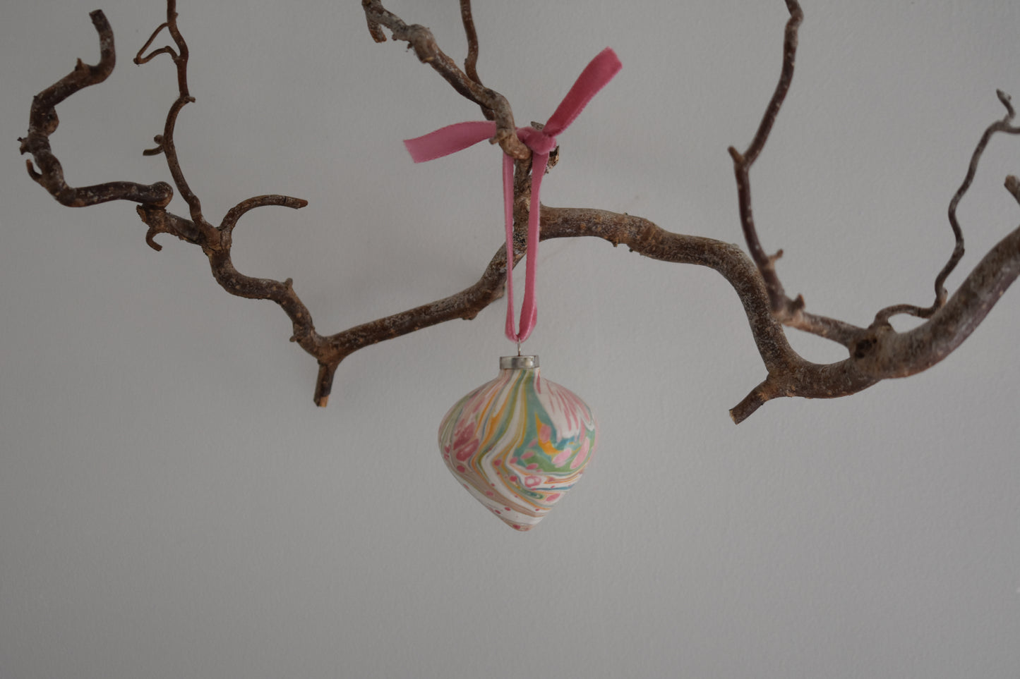 Jemma Lewis colourful marbled teardrop ceramic bauble Christmas ornament with velvet ribbon, hanging from a branch on a white background.