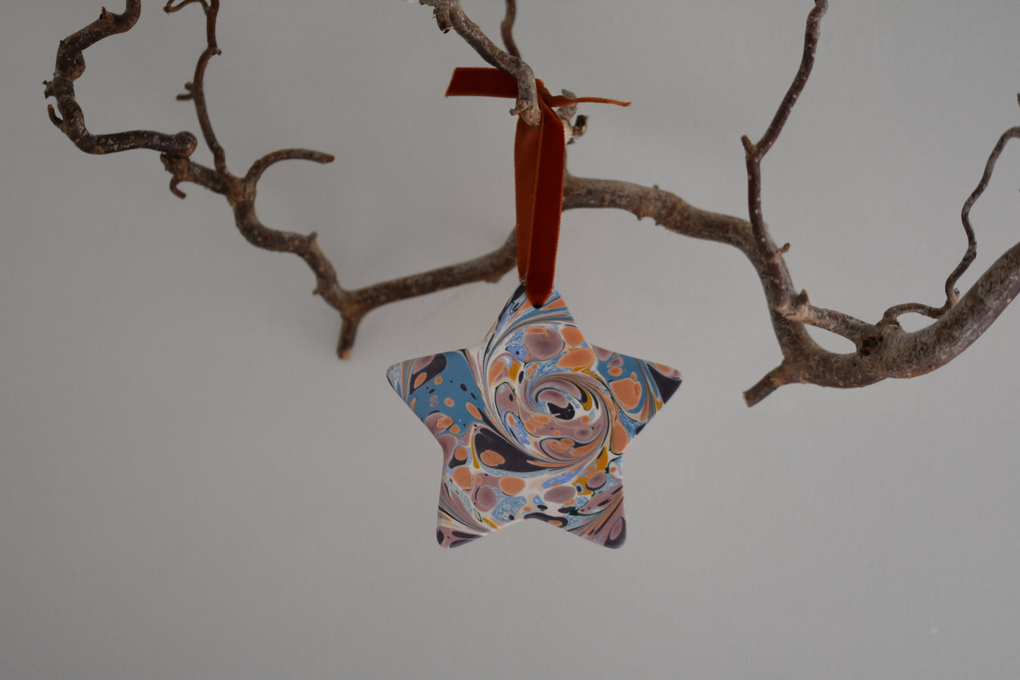 Jemma Lewis marbled ceramic star Christmas decoration ornament with colourful velvet ribbon, hanging from a branch on a white background.