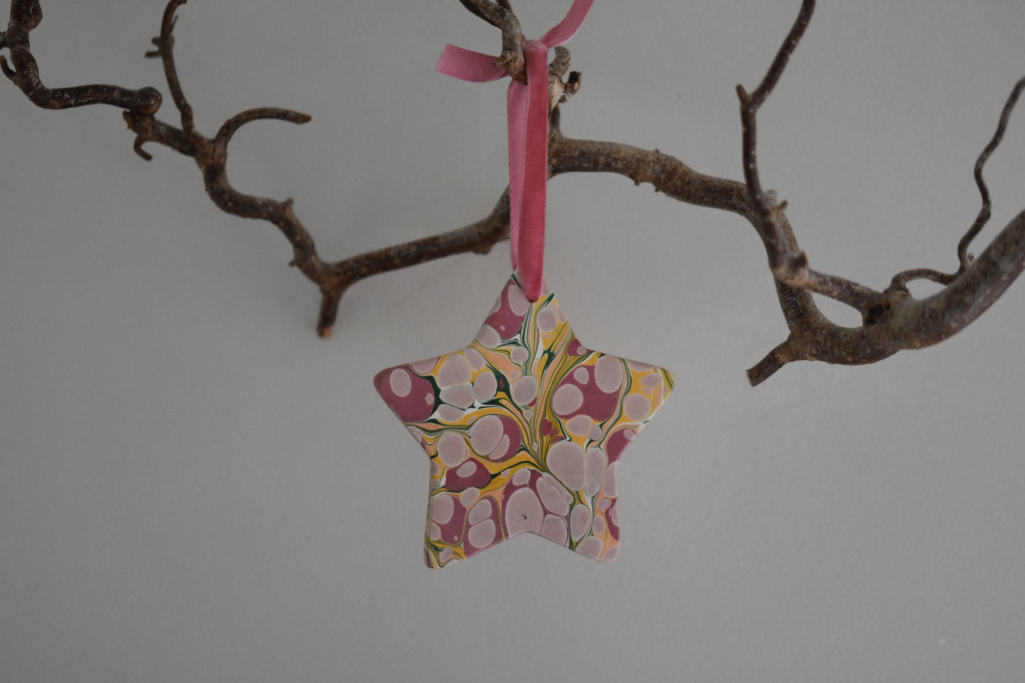 Jemma Lewis marbled ceramic star Christmas decoration ornament with colourful velvet ribbon, hanging from a branch on a white background.