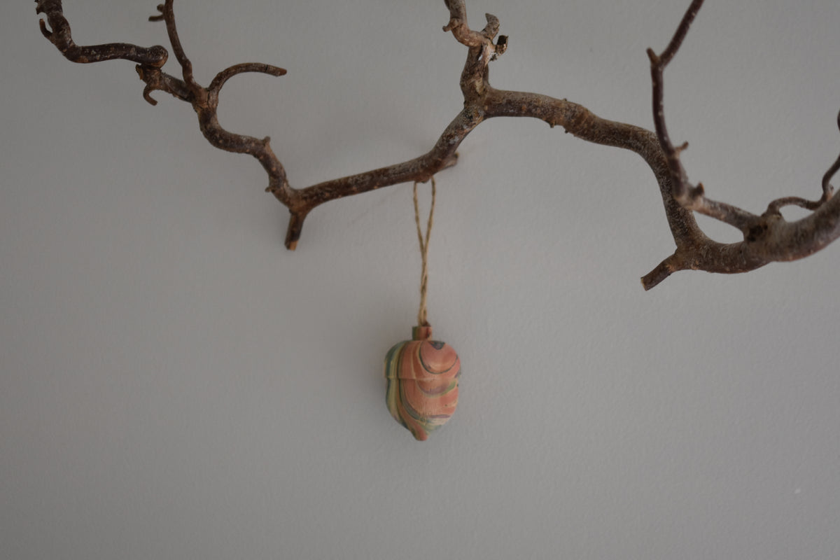 Jemma Lewis colourful marbled wooden acorn decoration Christmas ornament hung from twine on a branch, with a white background.