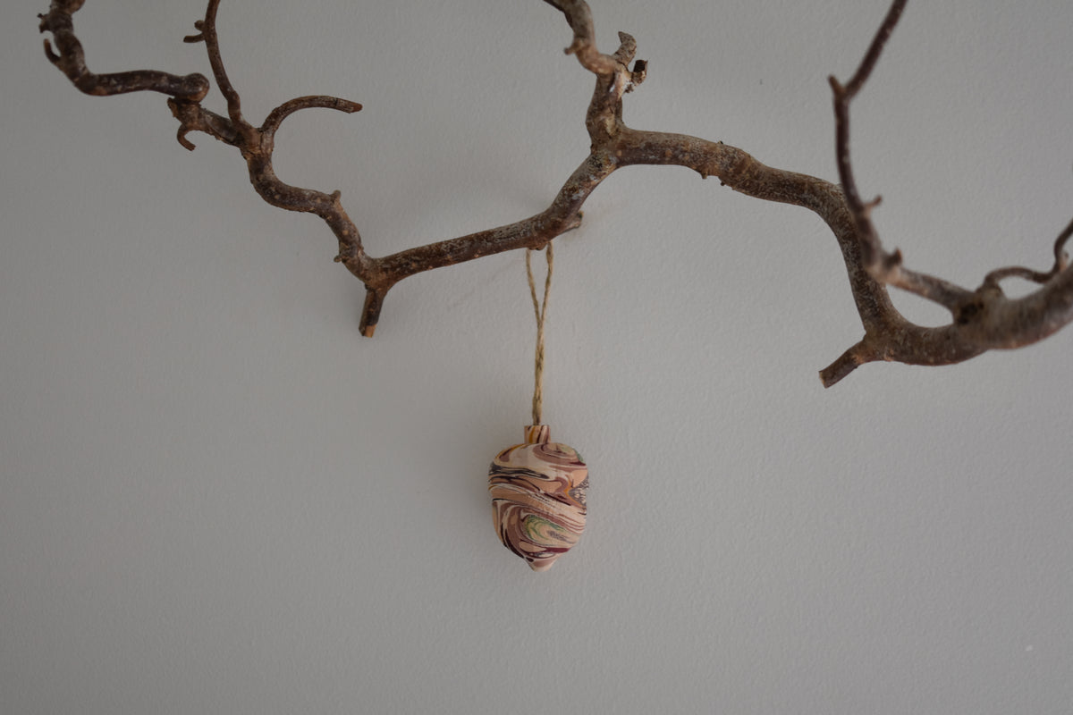 Jemma Lewis colourful marbled wooden acorn decoration Christmas ornament hung from twine on a branch, with a white background.