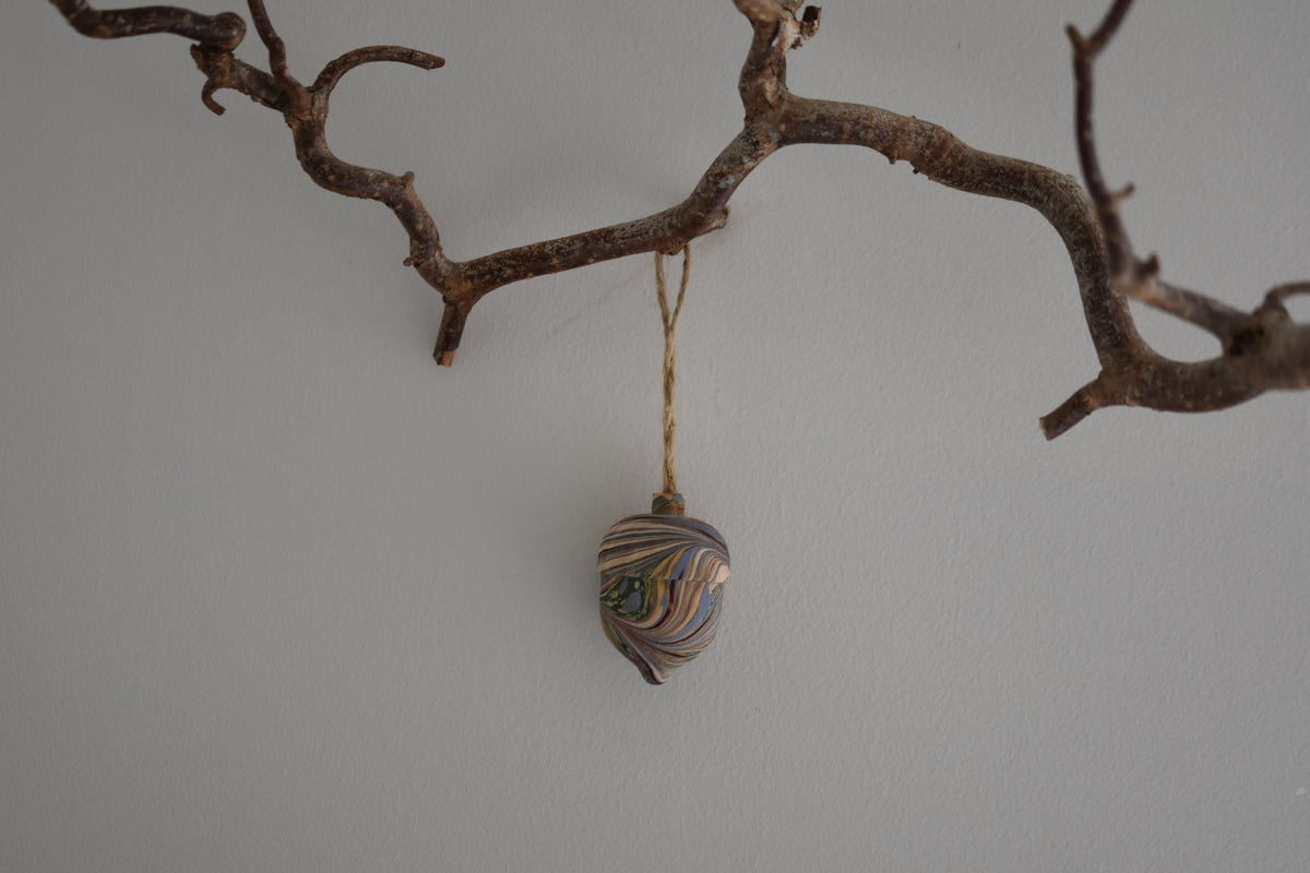 Jemma Lewis colourful marbled wooden acorn decoration Christmas ornament hung from twine on a branch, with a white background.