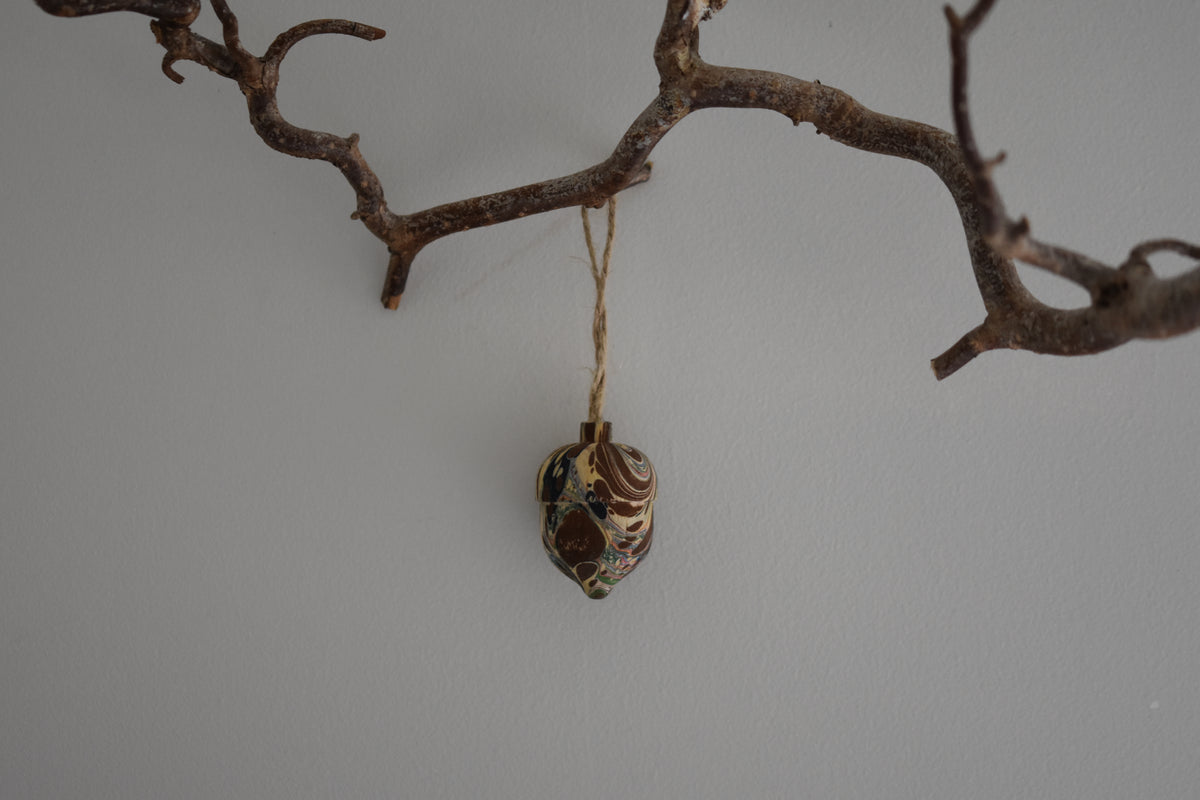 Jemma Lewis colourful marbled wooden acorn decoration Christmas ornament hung from twine on a branch, with a white background.