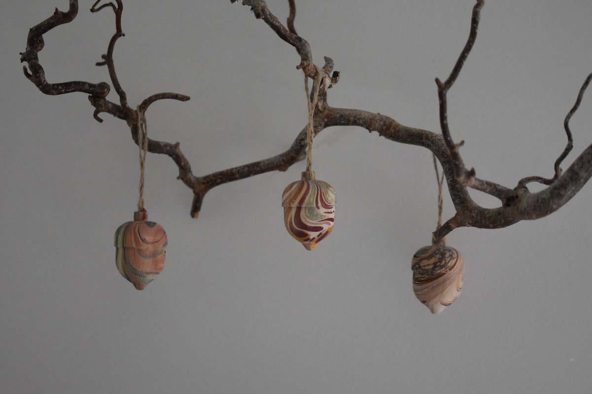 Jemma Lewis colourful marbled wooden acorn decoration Christmas ornaments hung on a branch with a white background.