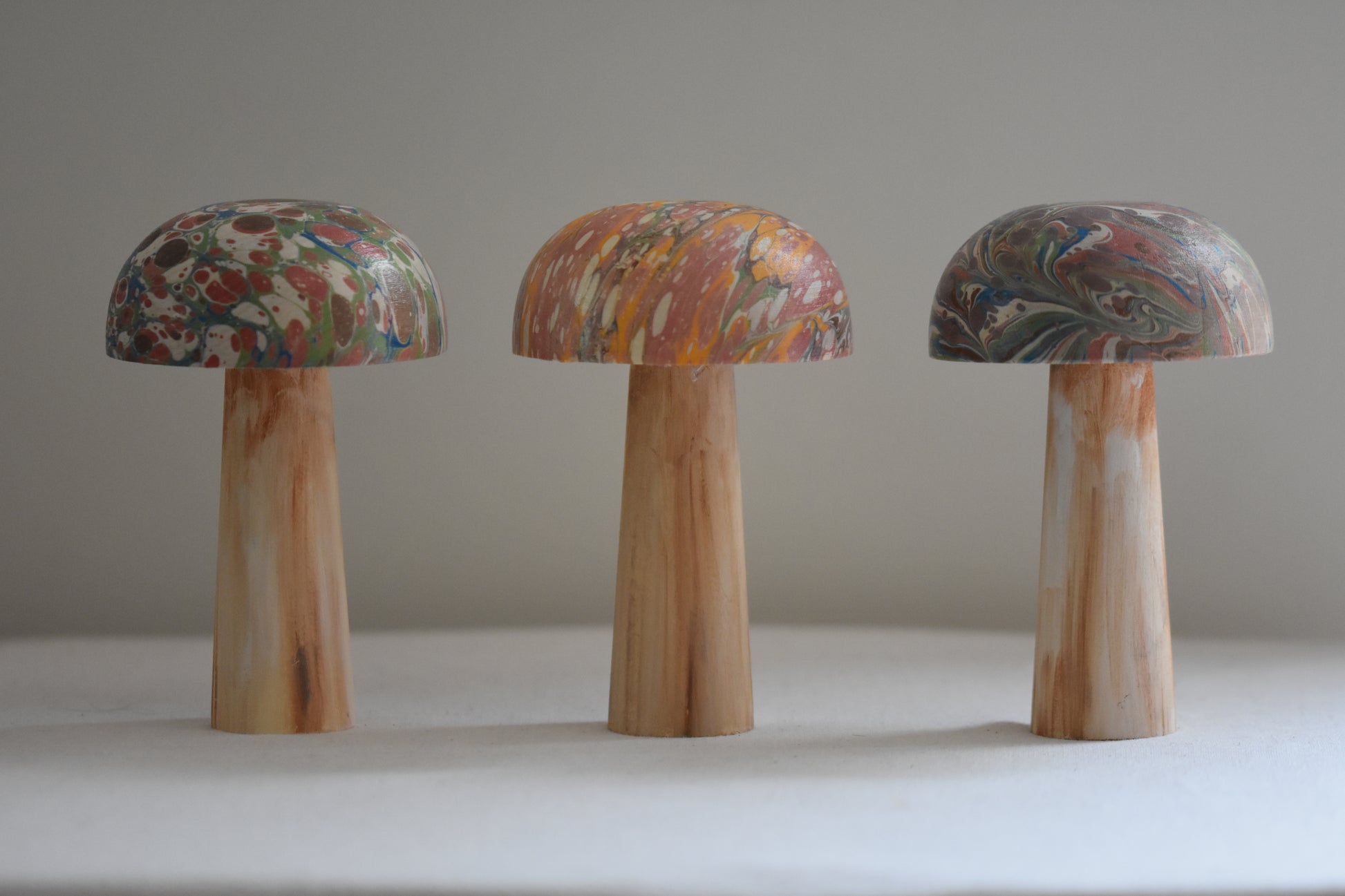 Jemma Lewis 3 marbled wooden decorative toadstool mushrooms figurines on a beige background.
