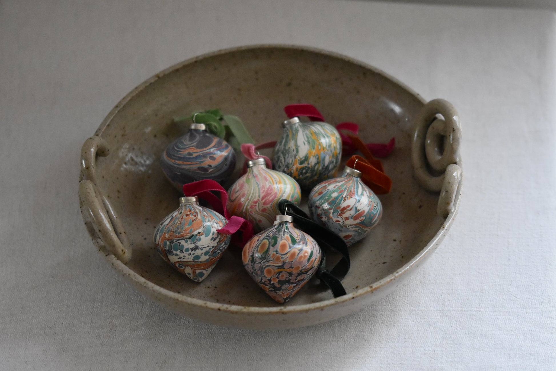 Jemma Lewis colourful marbled ceramic teardrop bauble Christmas ornaments with velvet ribbons, in a ceramic bowl on a beige background.